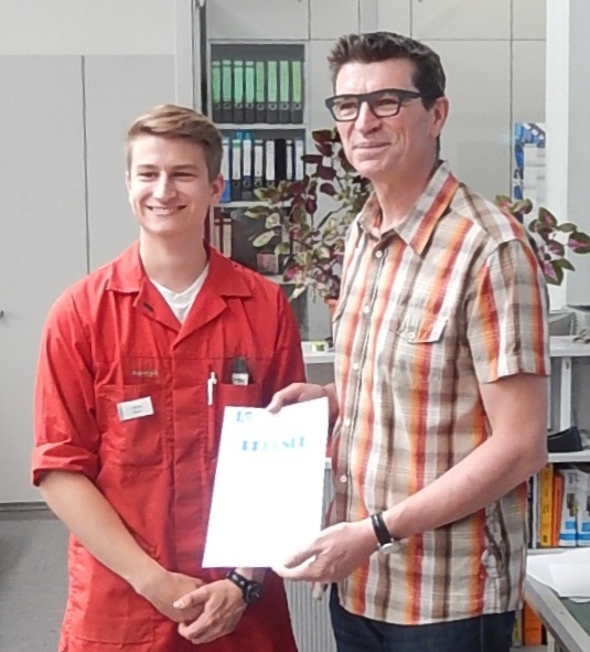 Schulleiter Thomas Ettwein übergibt die Urkunde und das Preisgeld an Tobias Kitzke für seinen Vorschlag, Schüler-Ersthelfer zu erfassen und auszuhängen.